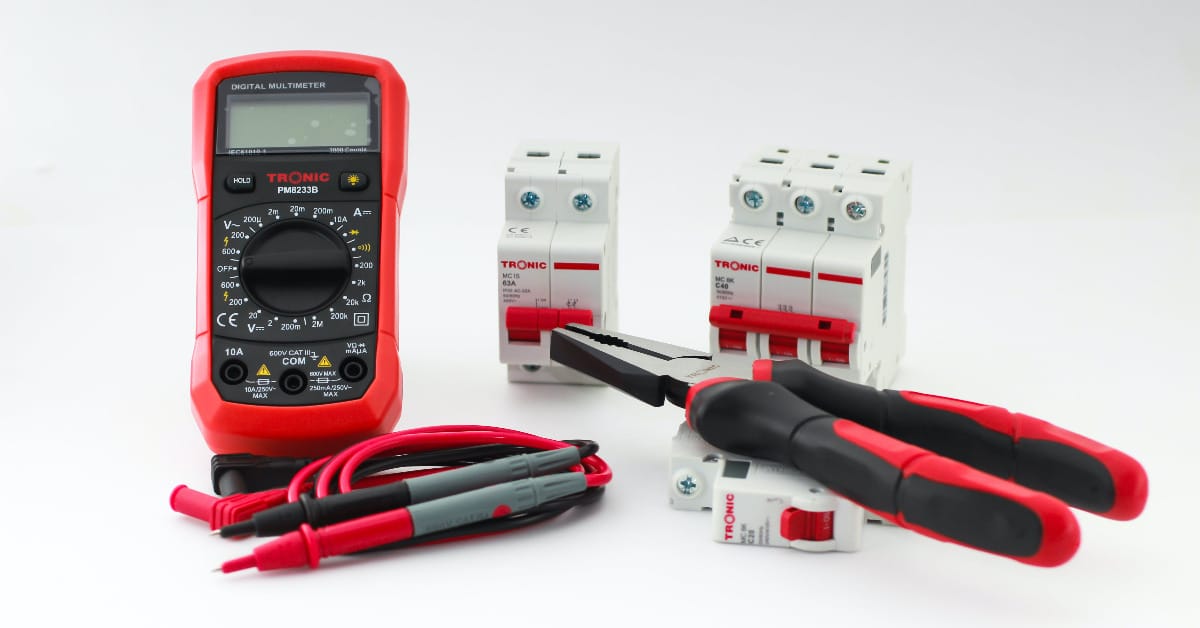 A multimeter, a circuit breakers and a pair of pliers on a white surface