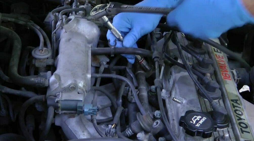 mechanic with blue glooves loosen the bolts that connect the fuel rail