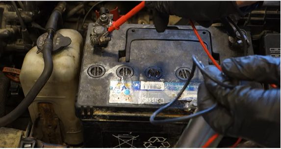 mechanic in black gloves holding red and black multimeter probe