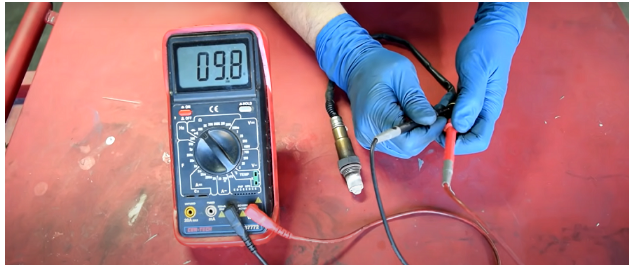 man in blue gloves testing the air fuel sensor with multimeter at a reading of 09.8v
