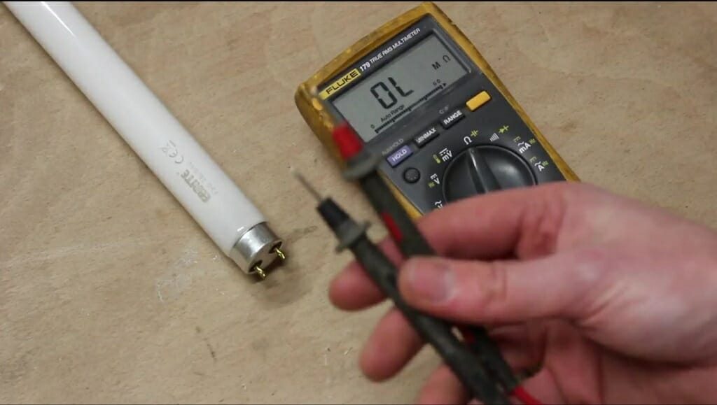 A technician holding the multimeter's red and black probe with multimeter and fluorescent tube light on the table