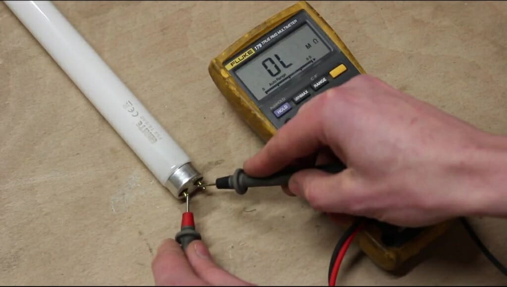 A technician testing florescent tube light on the table with multimeter at OL reading