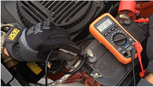 A mechanic with black gloves testing battery with multimeter