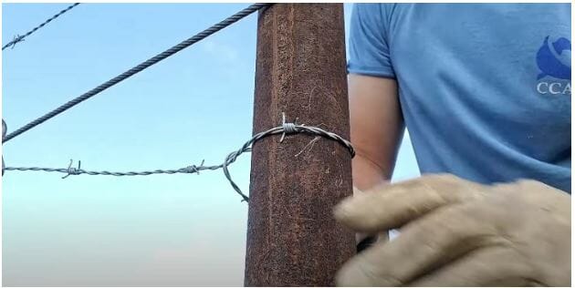 man wearing gloves and installing barbed wire fence on a post