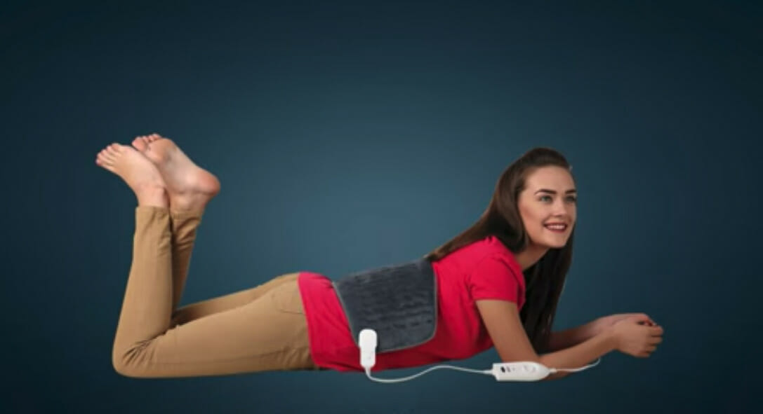a woman smiling and lying on her front with a heating pad on her lower back