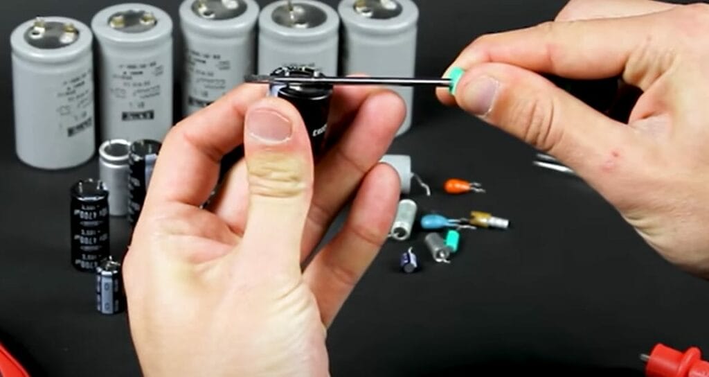 A person is shorting the capacitor using a screwdriver