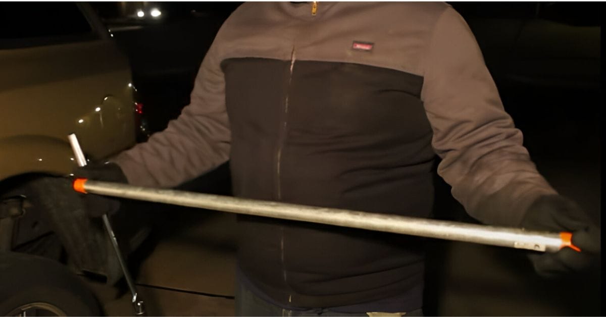 A man holding a breaker bar besides his car