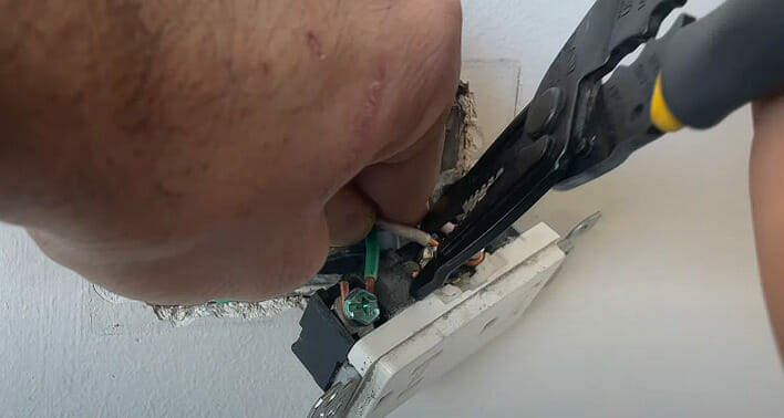 A person attaching the shiny new copper wire in its place and cutting extra wire