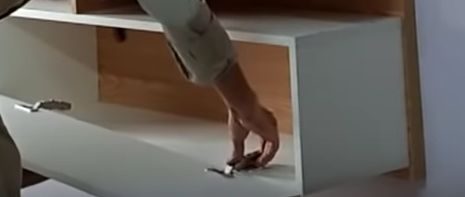 A woman is concealing wires behind a wall-mounted TV in a cabinet drawer