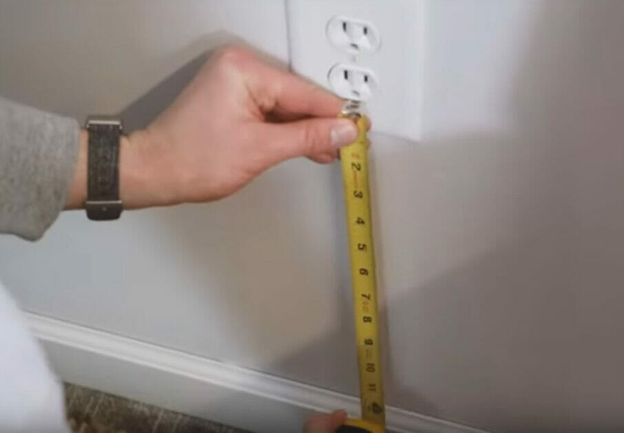 A person measures a wall outlet in order to hide wires for a wall-mounted TV