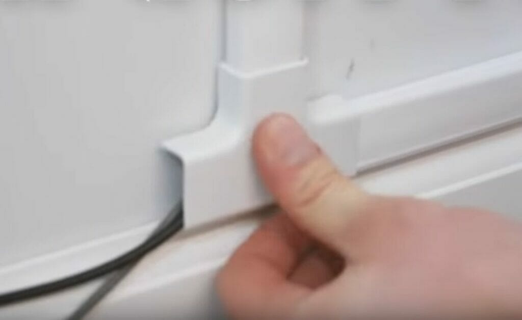 A person is concealing wires behind a conduit on a wall