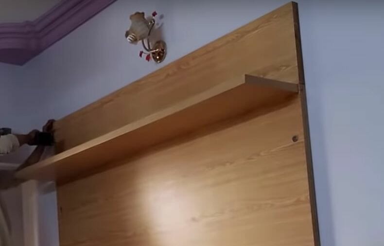 A man is installing a shelf on a wall, hiding wires for a wall-mounted TV cabinet