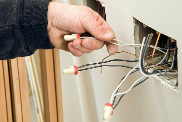 A person holding a wire from an undone outlet on the wall