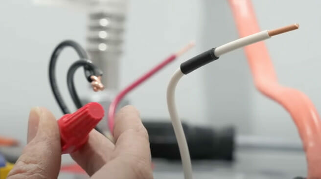 A person is holding a wire nut to connect the ends of the wire 