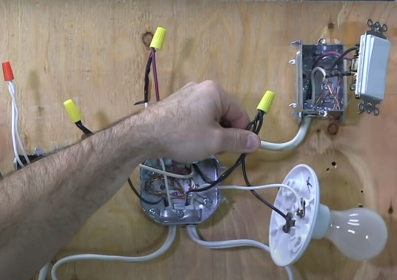 A person holding a black wire with yellow wire nut
