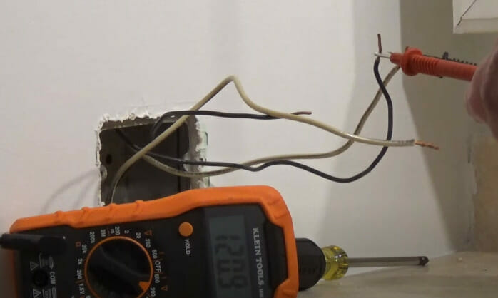 A person is testing a wire on the wall using multimeter