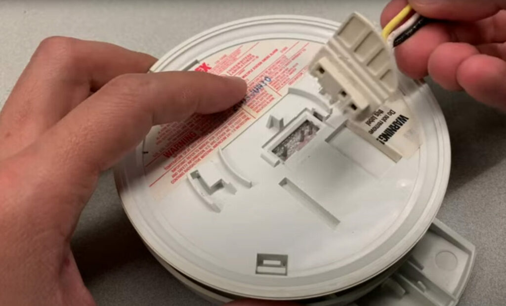 A person holding a detached smoke detector from the ceiling