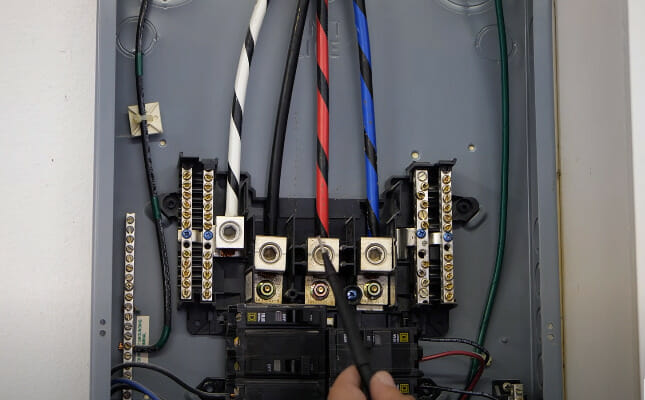 A person holding a black jumper infront of an electrical panel