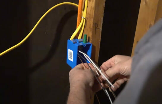 A man is wiring a blue box attached to the stud