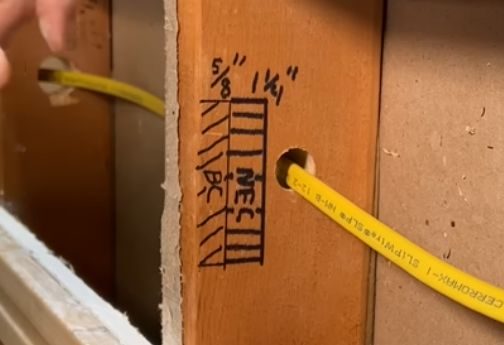 A person is using yellow tape to attach electrical wires to a cabinet in a wall
