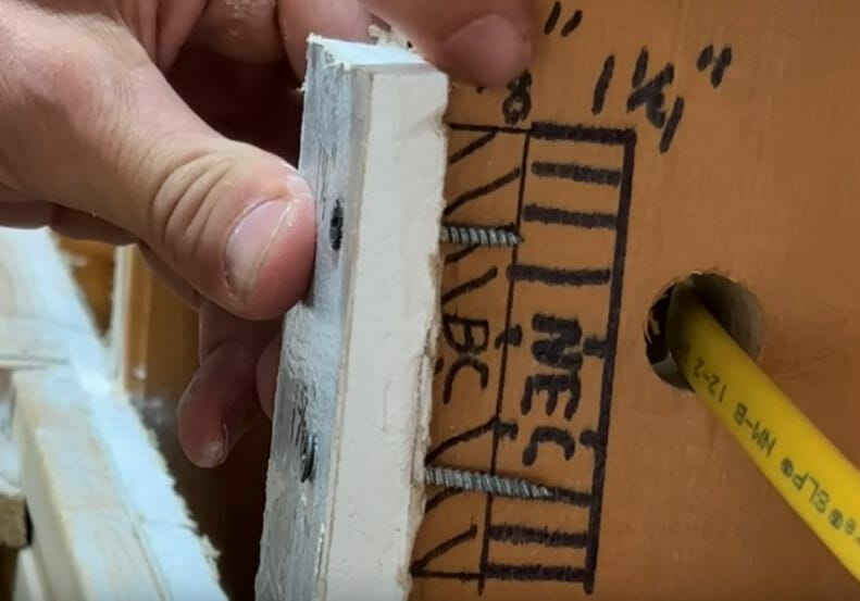 A person is using a screwdriver to attach a piece of wood to another piece of wood with wire