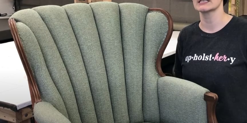 A woman is standing in front of a green chair that has an advanced tufting techniques