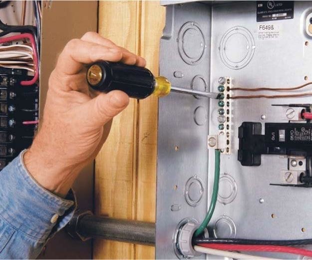 A man is using a screwdriver to fix a circuit breaker that has a ground wire issue