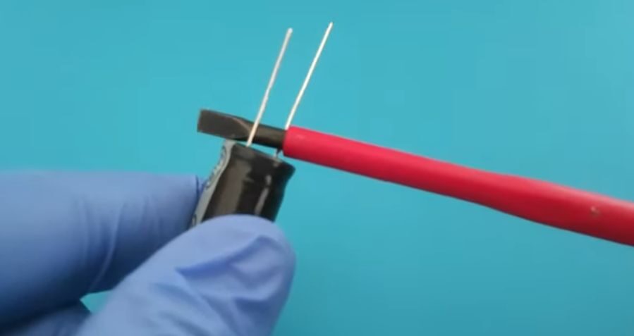 A person with gloves discharging a capacitor using a screwdriver