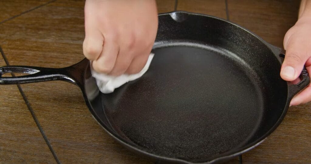 A person wiping the cast iron pan with clothe