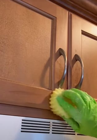 A person cleaning kitchen cabinets with a sponge to remove grease