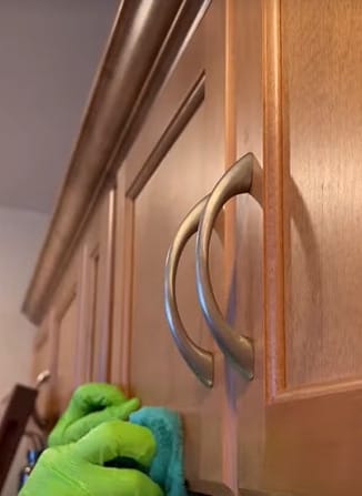 A person is cleaning a kitchen cabinet door to remove grease