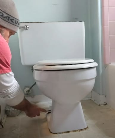 A person removing the bolts and nuts of the toilet base