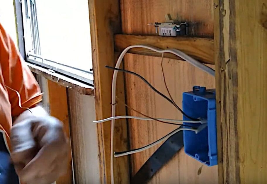 A man is installing an outlet wires in a blue electrical box attached to a wood stud