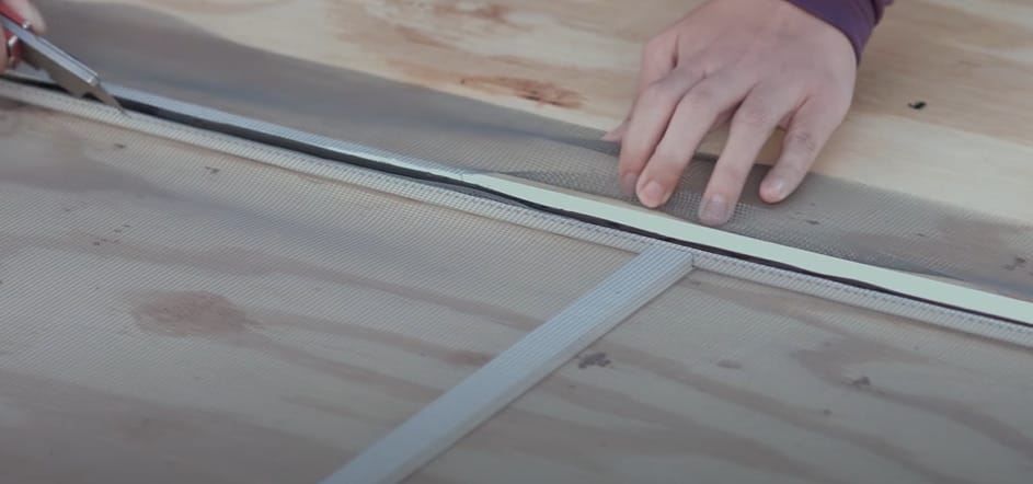 A person cutting the excess of a screen on a window