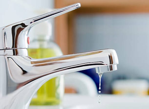 A close up image of a faucet with drop of water coming out in it