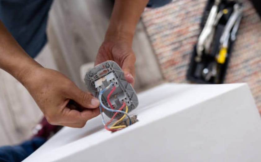 A person holding an electrical outlet with wires on a white table