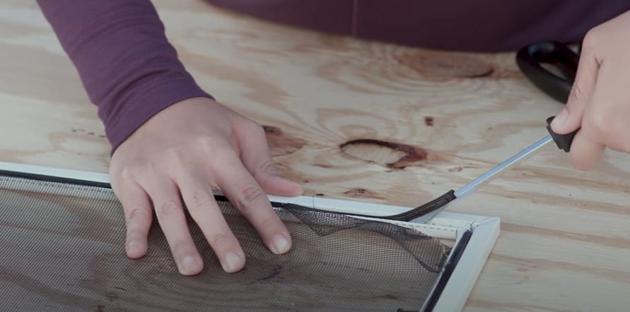 A person replacing a window screen