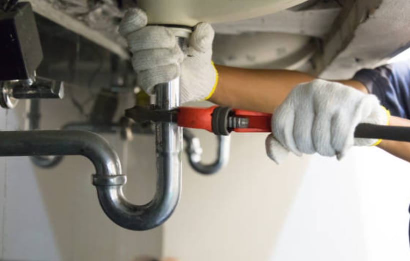 A plumber in gloves fixing a pipe under a sink