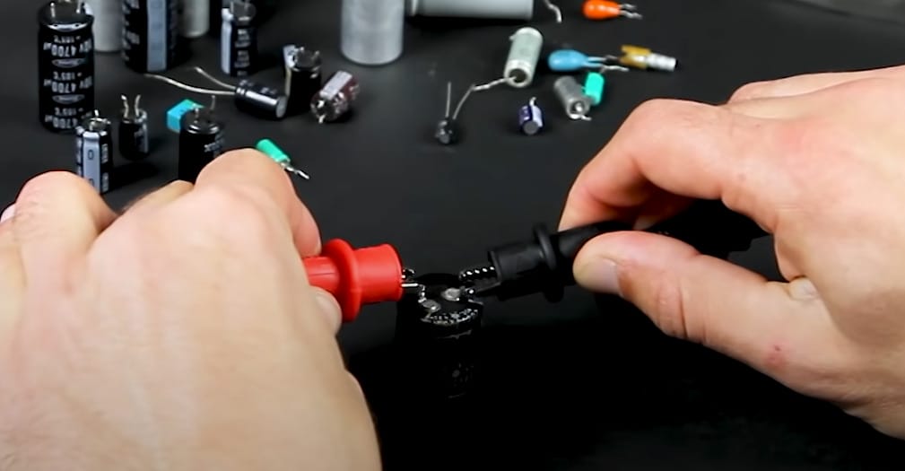 A person is connecting the multimeter leads to the capacitor's terminal for testing