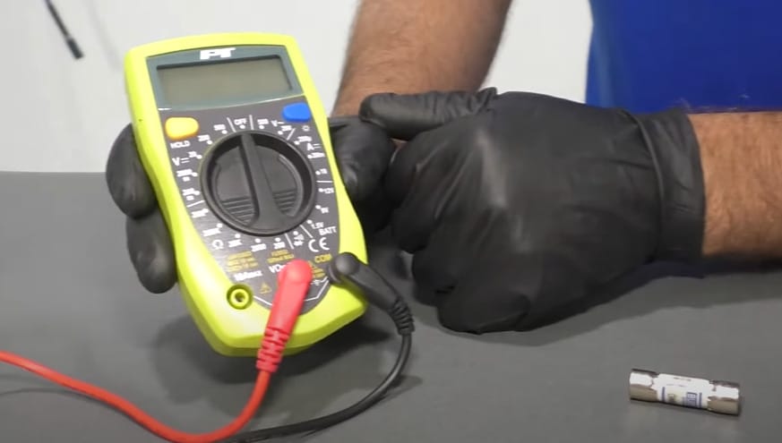 A person in black gloves holding a multimeter on the table