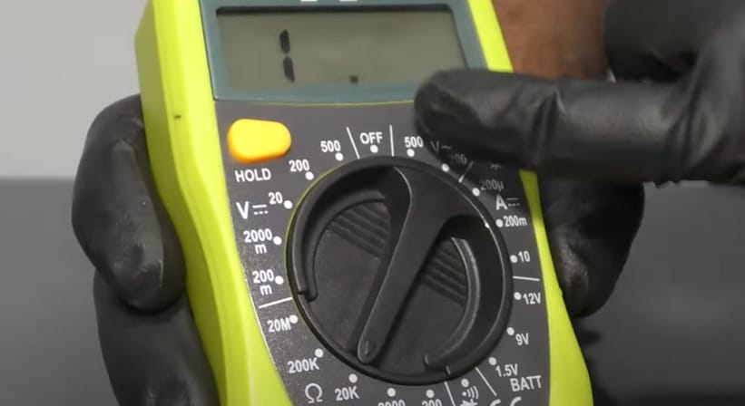 A person demonstrating how to test fuses using a multimeter while wearing black gloves