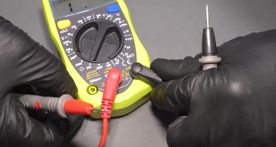 A person in black gloves connecting the probe into the multimeter