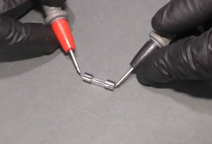 A person in black gloves testing a fuse with multimeter's probe