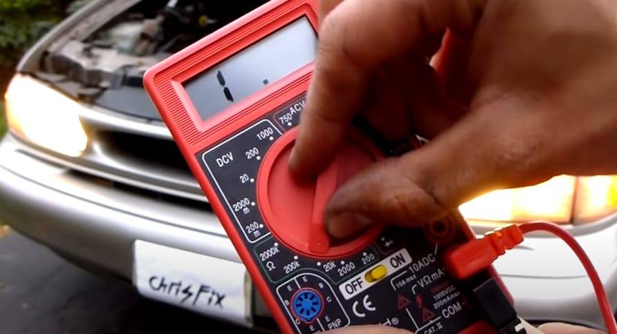 A person is setting up the red multimeter to test a car engine