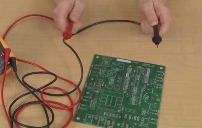 A person using a multimeter to check for continuity on a circuit board