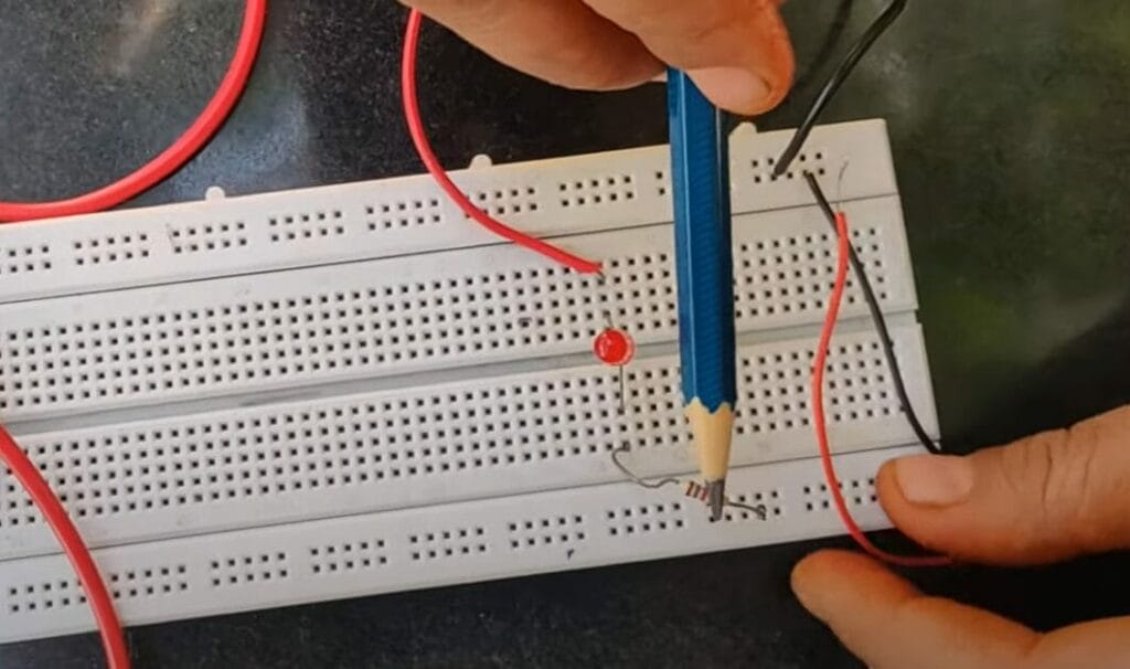 A person holding a pencil while working on a circuit board