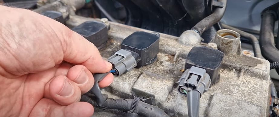 A person is checking the coil pack of a car