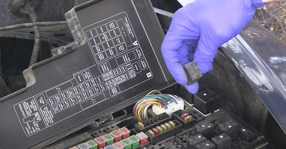 A person with purple gloves is working on a car's relay