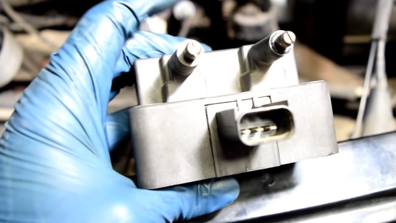 A person in blue gloves holding a car engine's coil pack