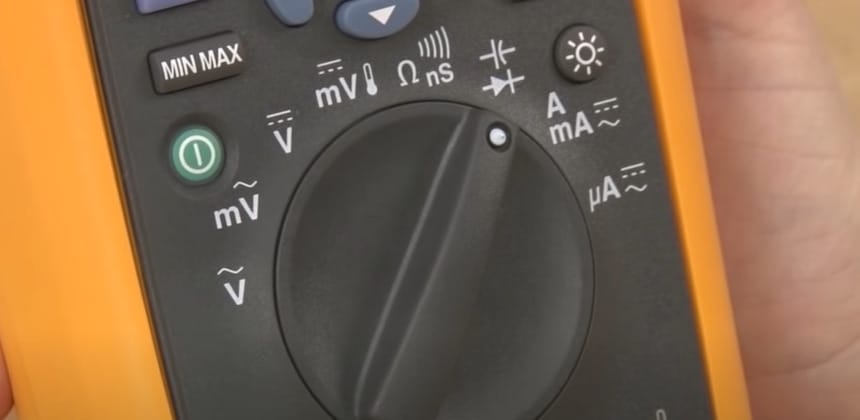 A person is holding a yellow multimeter, displaying the capacitance symbol on its screen